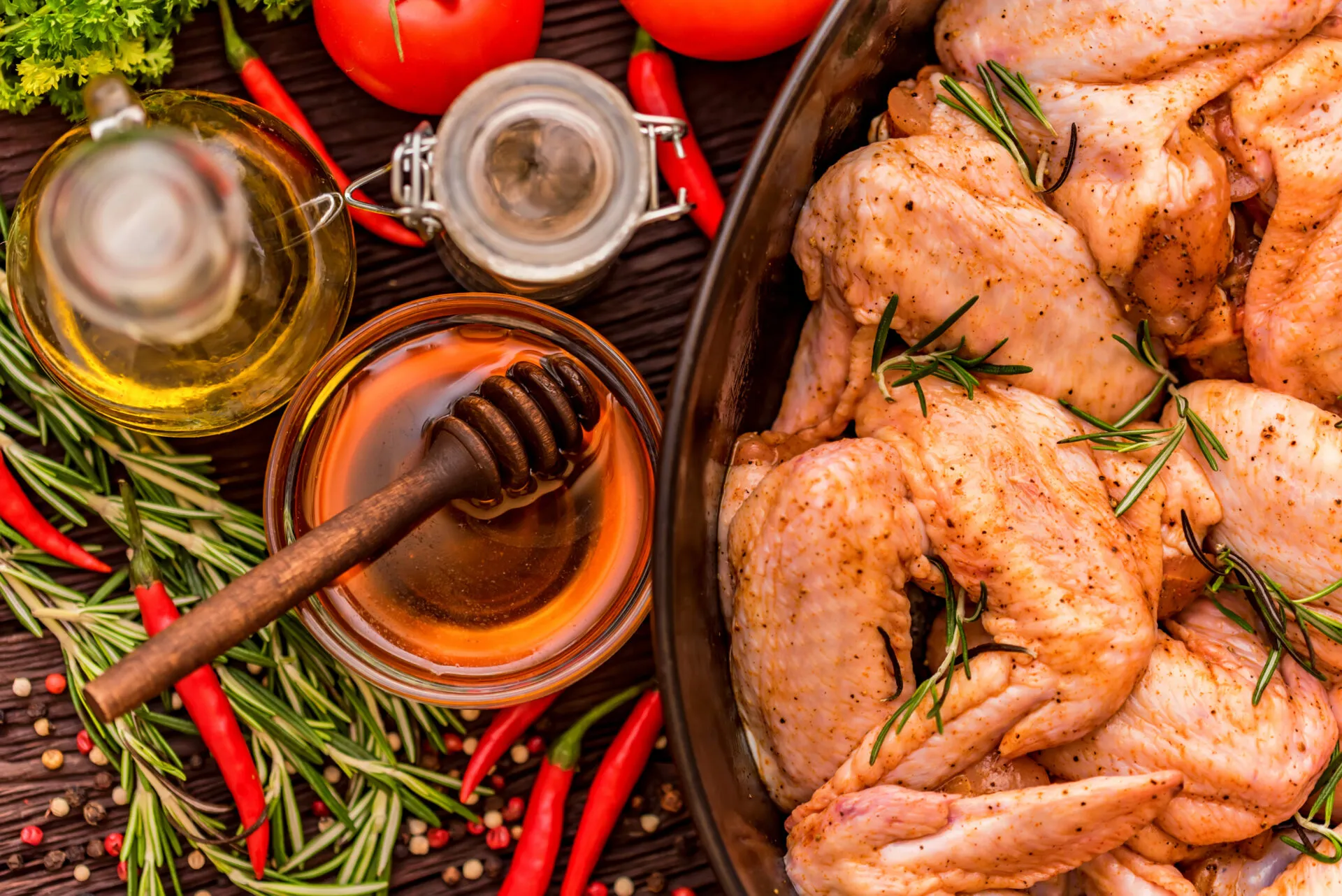 Pollo marinato con rosmarino e spezie, affiancato da miele, olio, peperoncini e pomodori.