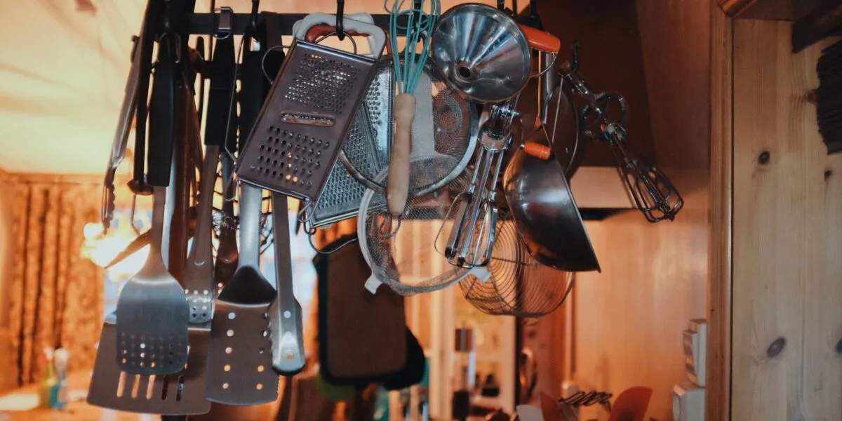 Utensili da cucina appesi e ammassati su una rastrelliera in una cucina rustica, simbolo di disordine e poco spazio.