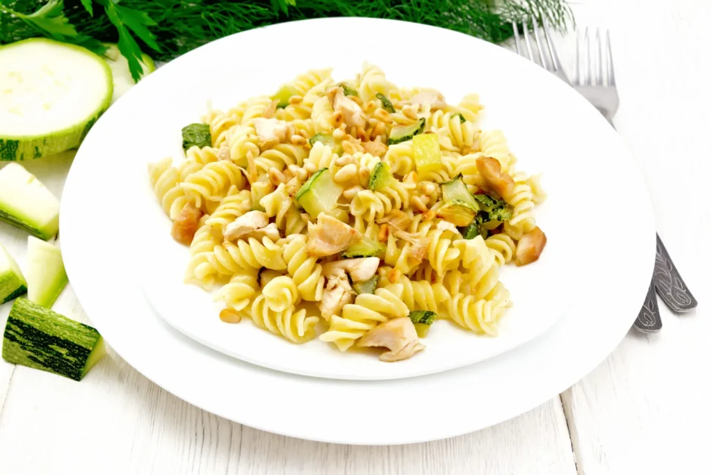 Pasta integrale con tonno, zucchine e pinoli servita in un piatto bianco.