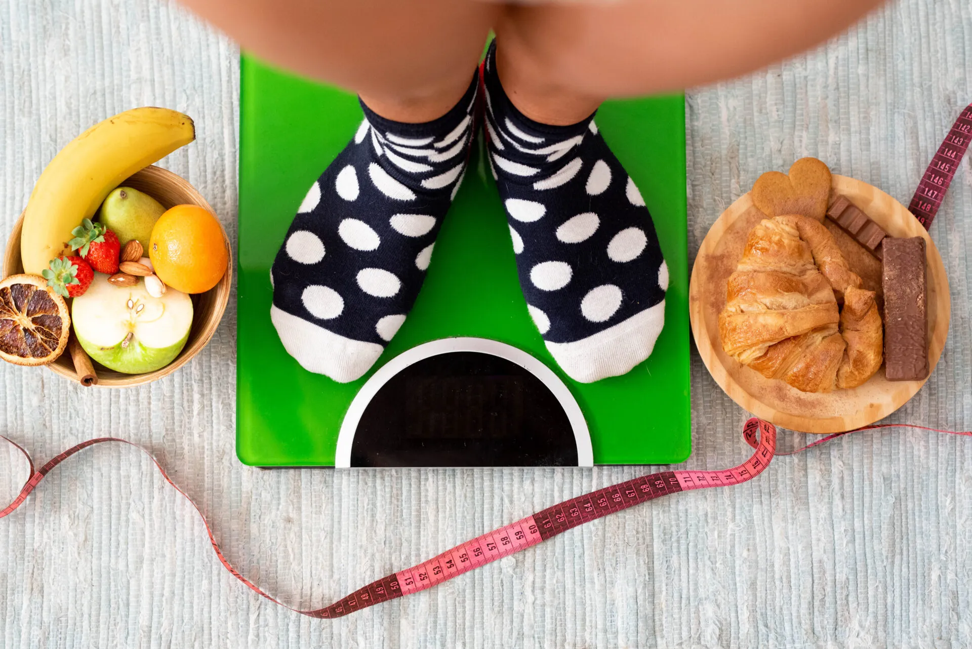 Persona sulla bilancia con a confronto alimenti sani e dolci, simbolo dello stallo del peso durante una dieta.