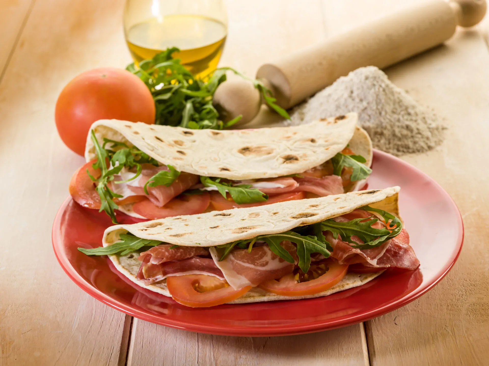 Piadine fit fatte in casa farcite con prosciutto crudo, pomodoro e rucola, servite su un piatto rosso.