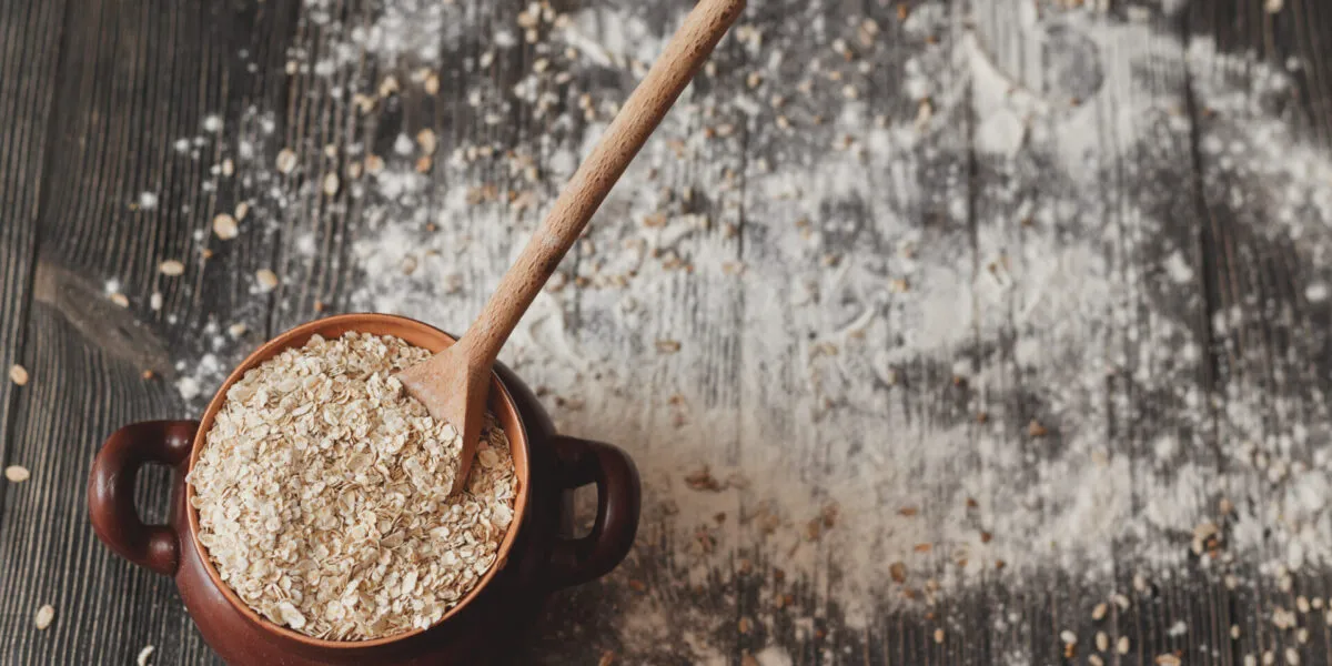 Ricette con avena: ciotola di fiocchi d’avena con cucchiaio su tavolo rustico e farina sparsa