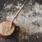 Ricette con avena: ciotola di fiocchi d’avena con cucchiaio su tavolo rustico e farina sparsa