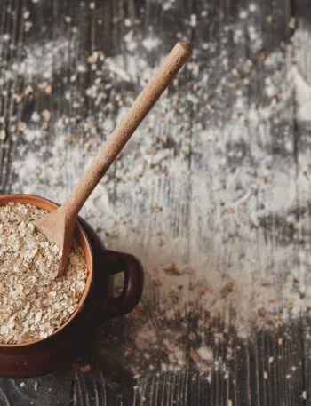 Ricette con avena: ciotola di fiocchi d’avena con cucchiaio su tavolo rustico e farina sparsa