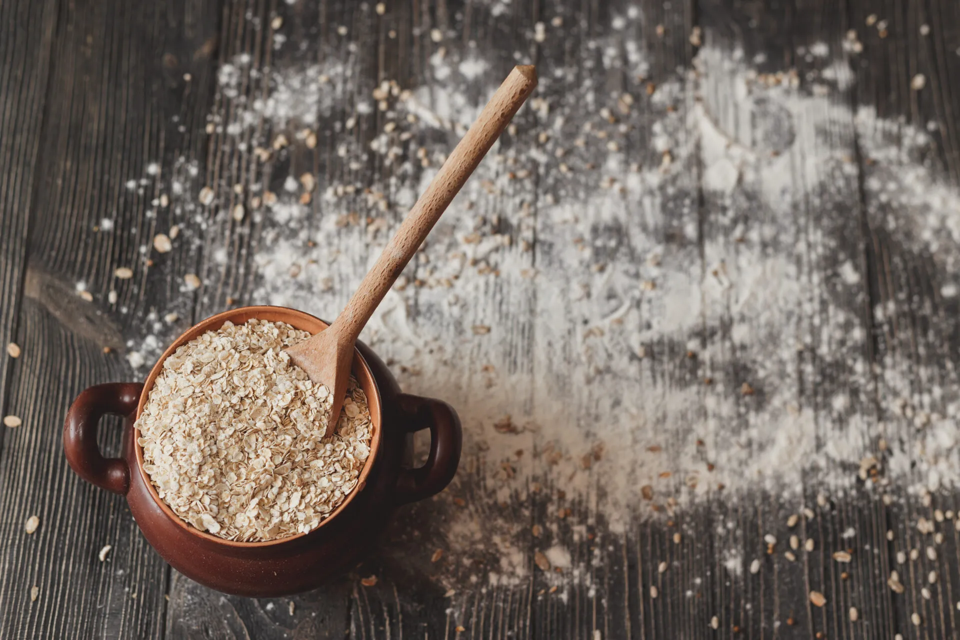 Ricette con avena: ciotola di fiocchi d’avena con cucchiaio su tavolo rustico e farina sparsa