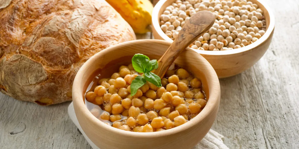 Ciotola di ceci cotti con basilico, accanto a pane rustico, zucca e ceci secchi.