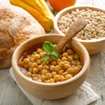 Ciotola di ceci cotti con basilico, accanto a pane rustico, zucca e ceci secchi.