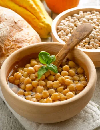 Ciotola di ceci cotti con basilico, accanto a pane rustico, zucca e ceci secchi.