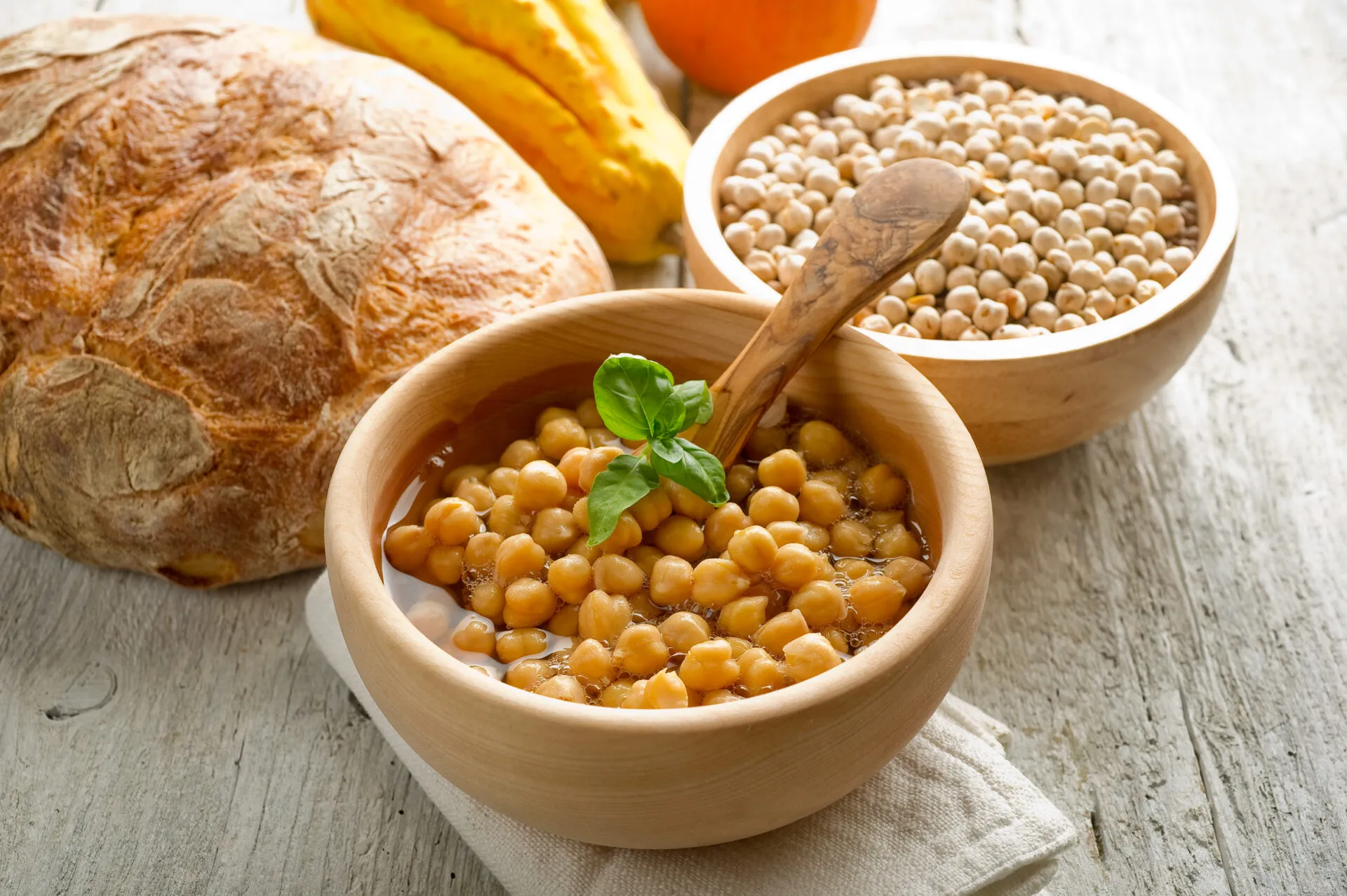 Ciotola di ceci cotti con basilico, accanto a pane rustico, zucca e ceci secchi.