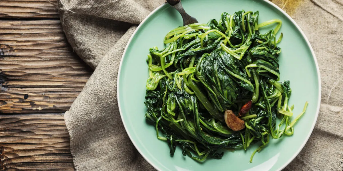 Spinaci saltati in padella con aglio e peperoncino serviti in un piatto verde su tavolo di legno.