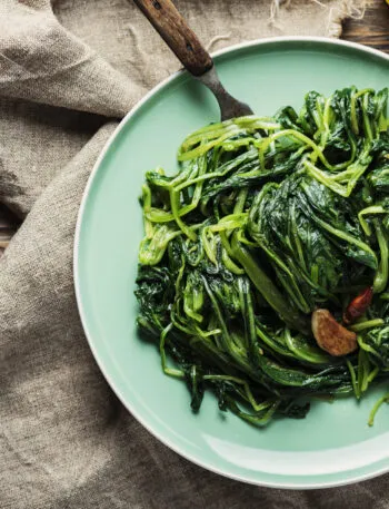 Spinaci saltati in padella con aglio e peperoncino serviti in un piatto verde su tavolo di legno.