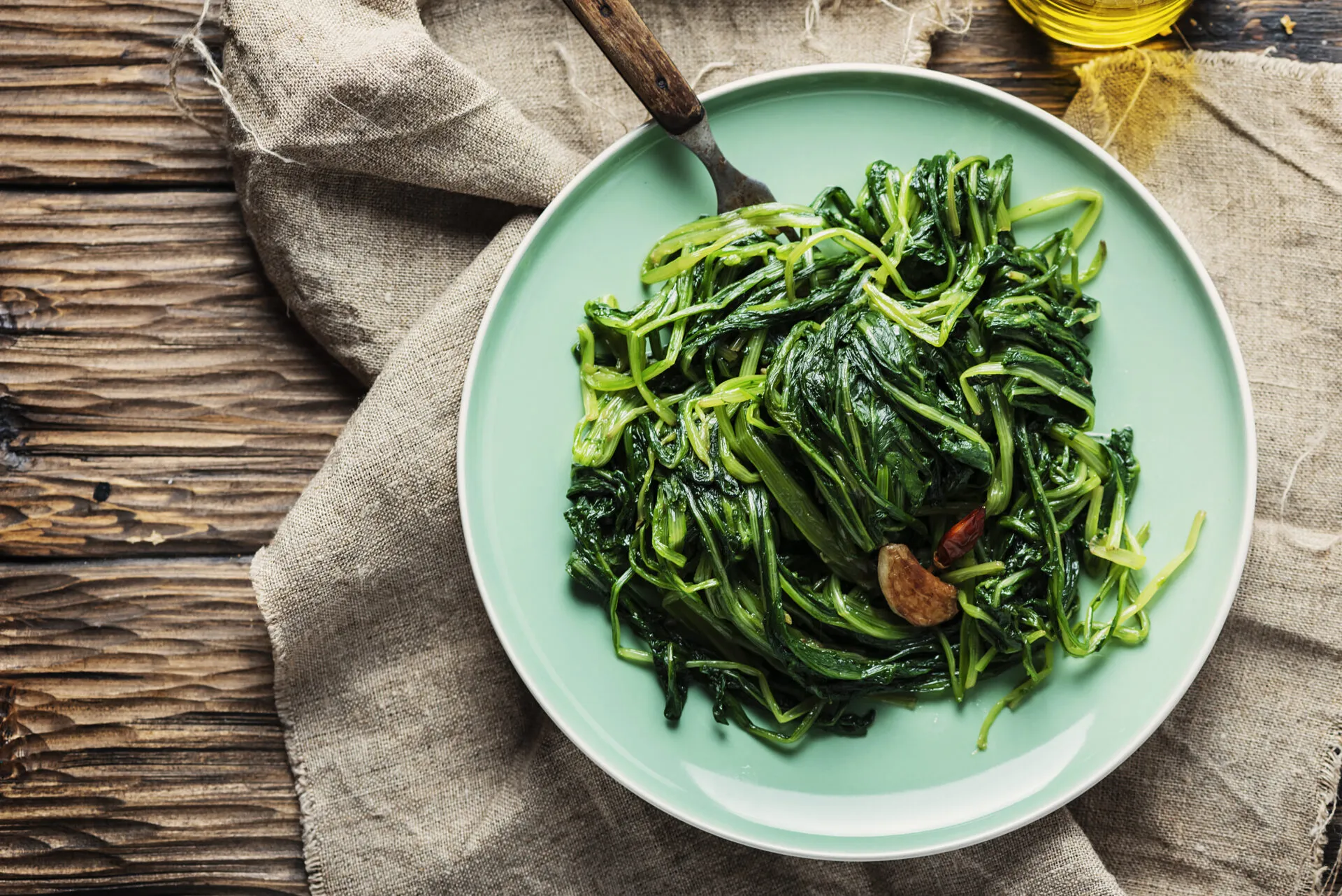 Spinaci saltati in padella con aglio e peperoncino serviti in un piatto verde su tavolo di legno.