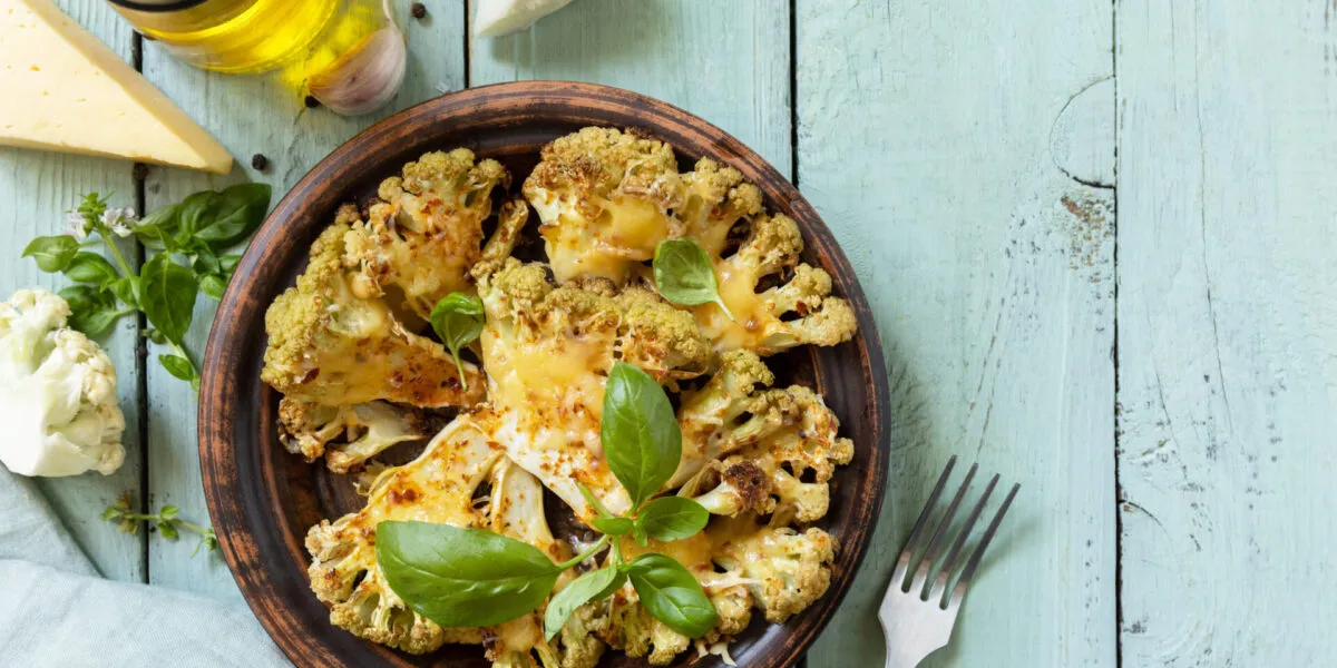 Cavolfiore gratinato al forno con formaggio e basilico, servito in un piatto rustico su tavolo azzurro.