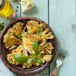 Cavolfiore gratinato al forno con formaggio e basilico, servito in un piatto rustico su tavolo azzurro.