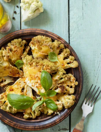 Cavolfiore gratinato al forno con formaggio e basilico, servito in un piatto rustico su tavolo azzurro.