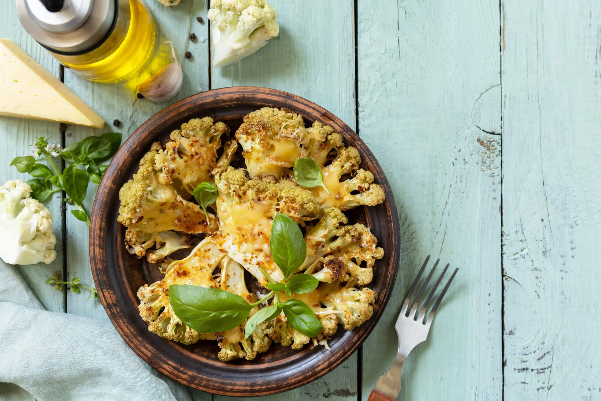 Cavolfiore gratinato al forno con formaggio e basilico, servito in un piatto rustico su tavolo azzurro.