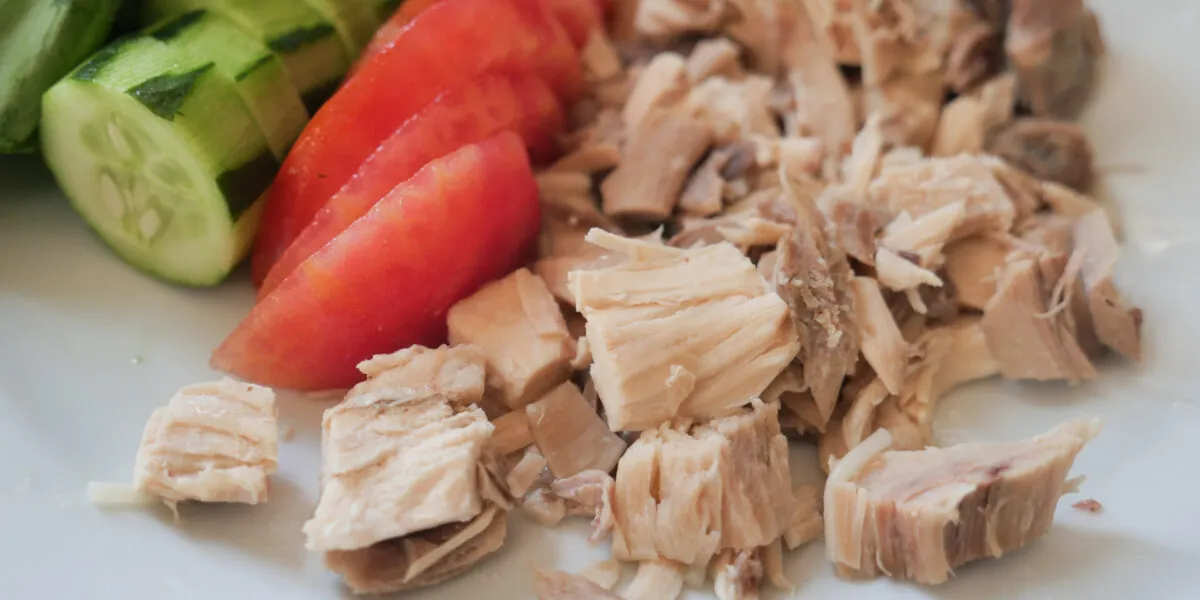 Tonno al naturale sgocciolato con pomodori e cetrioli freschi su un piatto bianco.
