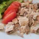 Tonno al naturale sgocciolato con pomodori e cetrioli freschi su un piatto bianco.