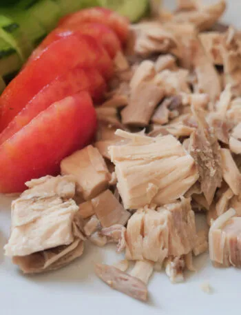 Tonno al naturale sgocciolato con pomodori e cetrioli freschi su un piatto bianco.