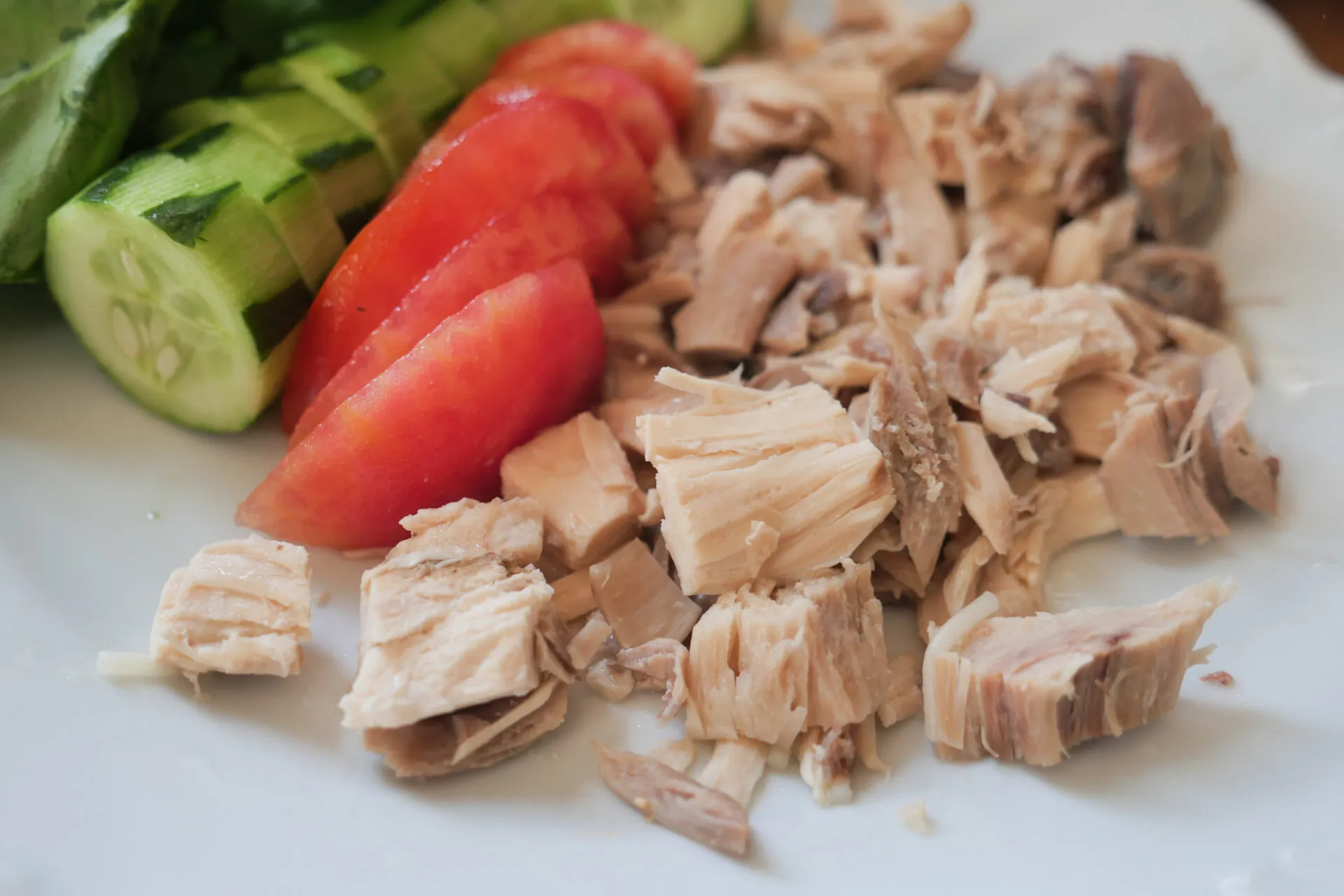 Tonno al naturale sgocciolato con pomodori e cetrioli freschi su un piatto bianco.