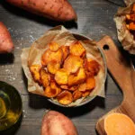 Patate dolci intere, a rondelle croccanti e a bastoncino su un tavolo in legno, con olio e sale grosso.