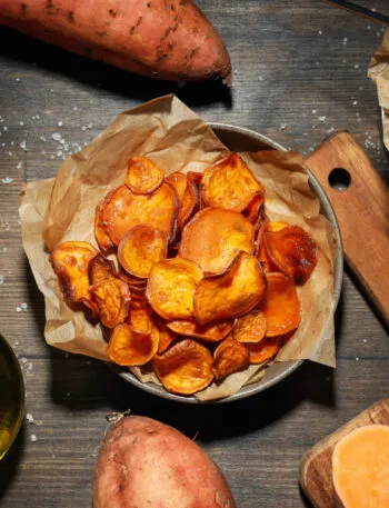 Patate dolci intere, a rondelle croccanti e a bastoncino su un tavolo in legno, con olio e sale grosso.
