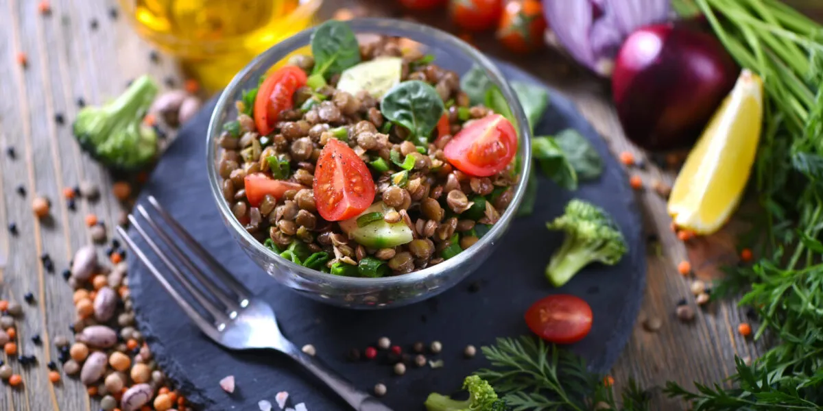 Insalata fit di lenticchie con pomodorini, cetriolo e spinaci, servita in una ciotola di vetro con verdure fresche.