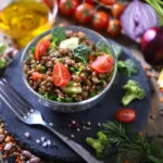 Insalata fit di lenticchie con pomodorini, cetriolo e spinaci, servita in una ciotola di vetro con verdure fresche.