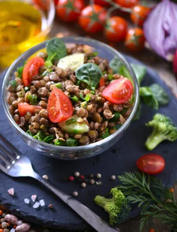 Insalata fit di lenticchie con pomodorini, cetriolo e spinaci, servita in una ciotola di vetro con verdure fresche.