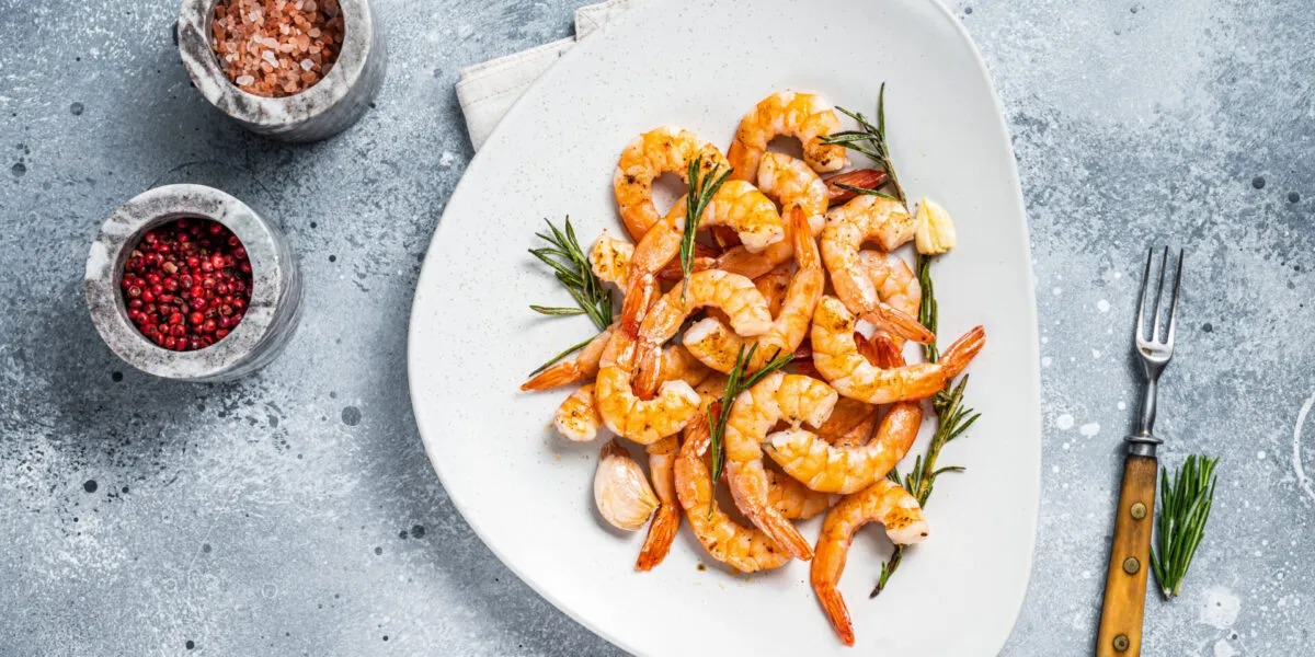 Gamberi alla griglia con rosmarino, aglio e limone serviti su un piatto bianco.
