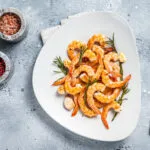Gamberi alla griglia con rosmarino, aglio e limone serviti su un piatto bianco.
