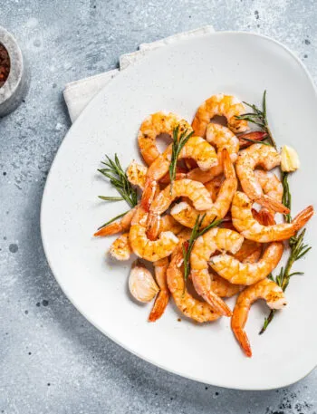Gamberi alla griglia con rosmarino, aglio e limone serviti su un piatto bianco.