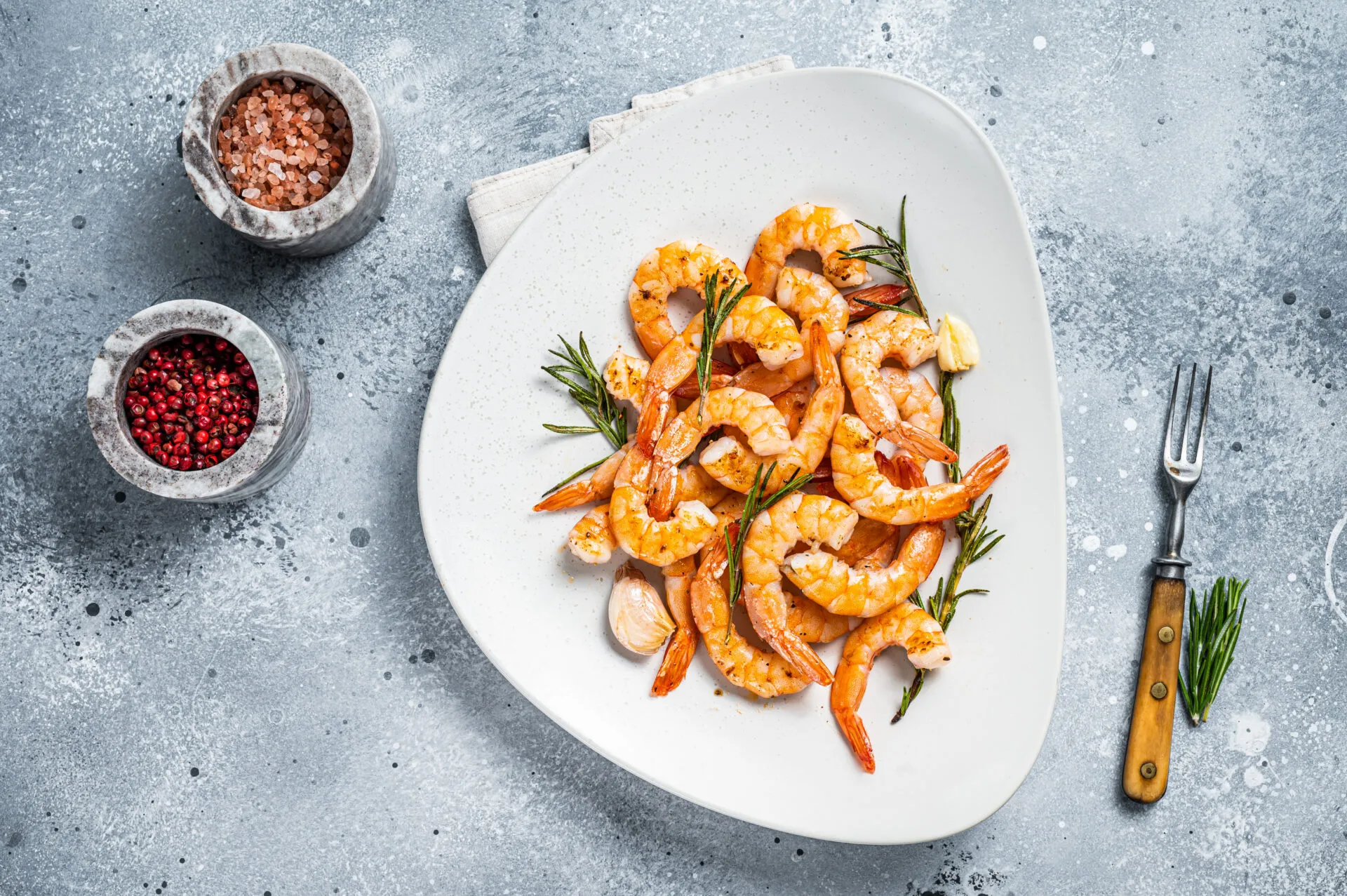 Gamberi alla griglia con rosmarino, aglio e limone serviti su un piatto bianco.