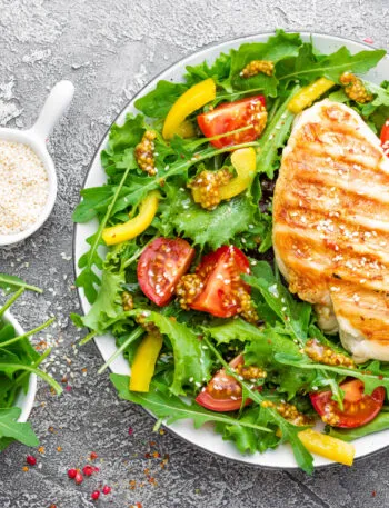 Petto di pollo grigliato su insalata di rucola, pomodorini e peperoni gialli con semi di sesamo.