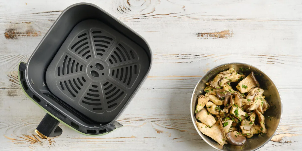Friggitrice ad aria aperta con ciotola di funghi conditi su un tavolo in legno bianco.