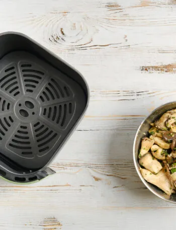 Friggitrice ad aria aperta con ciotola di funghi conditi su un tavolo in legno bianco.
