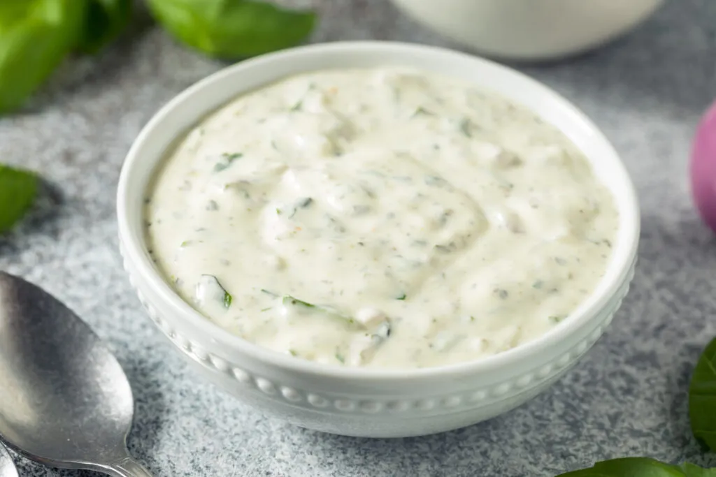 Salsa allo yogurt fit fatta in casa in ciotola bianca con erbe aromatiche su fondo grigio.