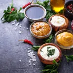 Salse fit fatte in casa in ciotole con ketchup, maionese, senape, yogurt, spezie ed erbe aromatiche su fondo scuro.