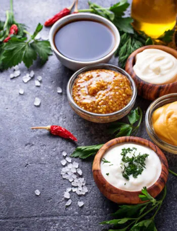 Salse fit fatte in casa in ciotole con ketchup, maionese, senape, yogurt, spezie ed erbe aromatiche su fondo scuro.
