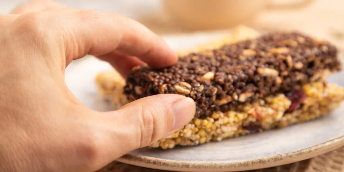 Mano che prende una barretta proteica al cioccolato sopra una barretta ai cereali e frutta secca.