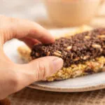 Mano che prende una barretta proteica al cioccolato sopra una barretta ai cereali e frutta secca.