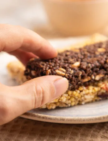 Mano che prende una barretta proteica al cioccolato sopra una barretta ai cereali e frutta secca.