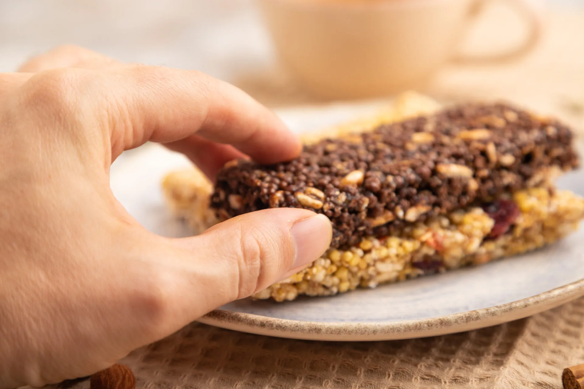 Mano che prende una barretta proteica al cioccolato sopra una barretta ai cereali e frutta secca.