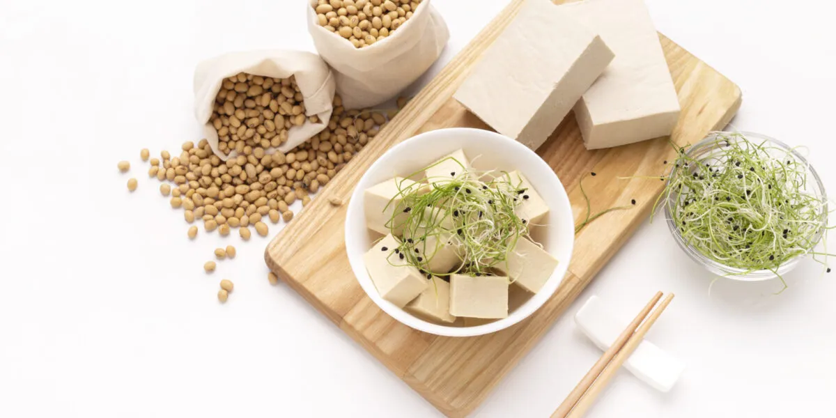 Tofu a cubetti e in panetti con germogli e semi di soia su un tagliere di legno.