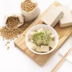 Tofu a cubetti e in panetti con germogli e semi di soia su un tagliere di legno.