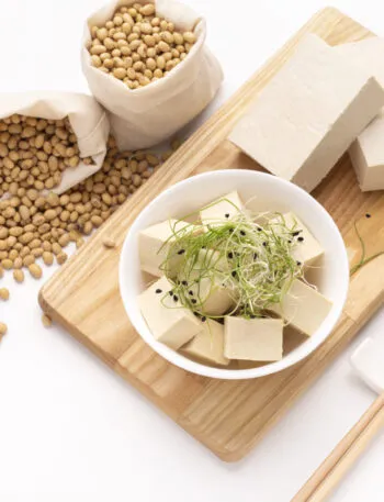 Tofu a cubetti e in panetti con germogli e semi di soia su un tagliere di legno.