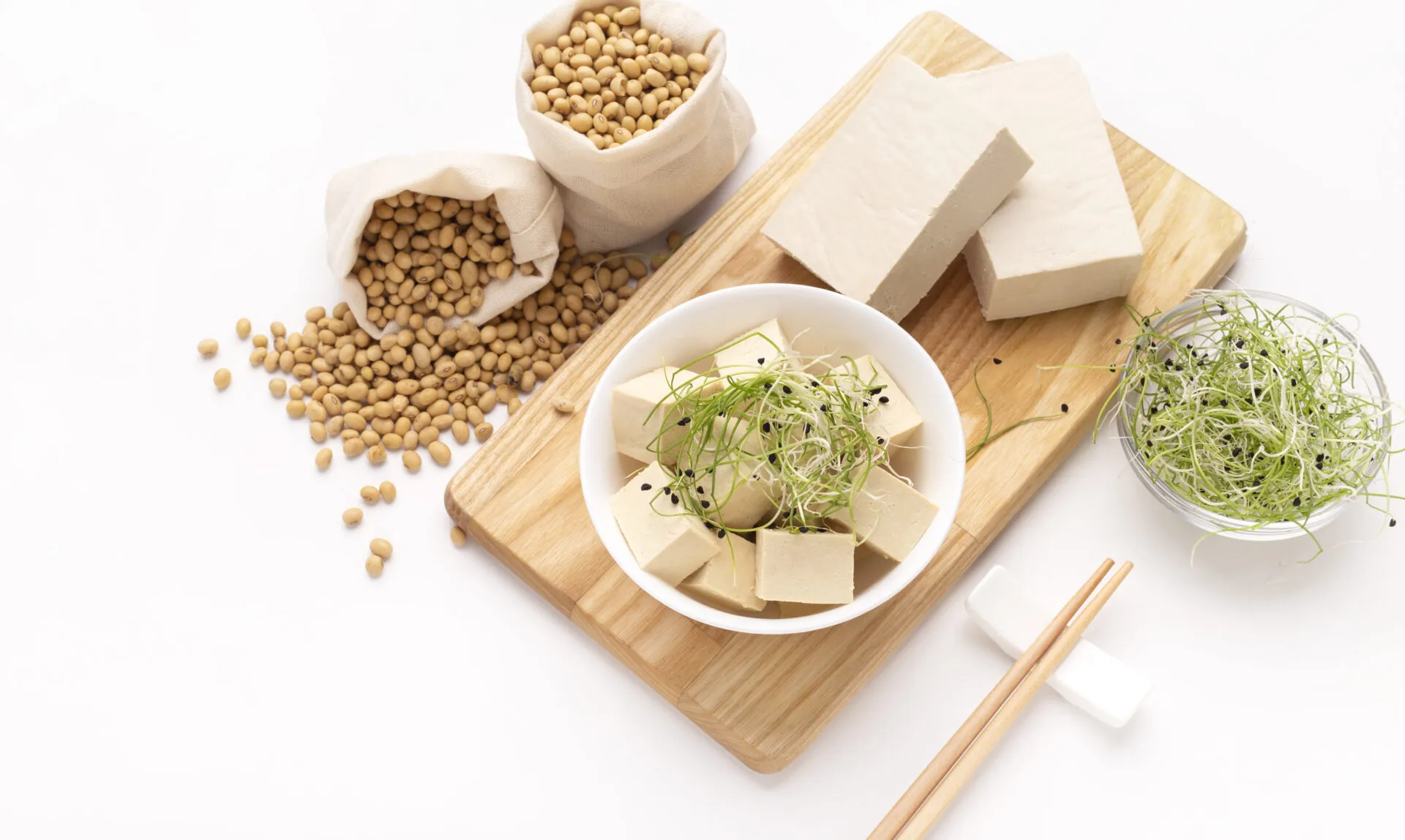 Tofu a cubetti e in panetti con germogli e semi di soia su un tagliere di legno.