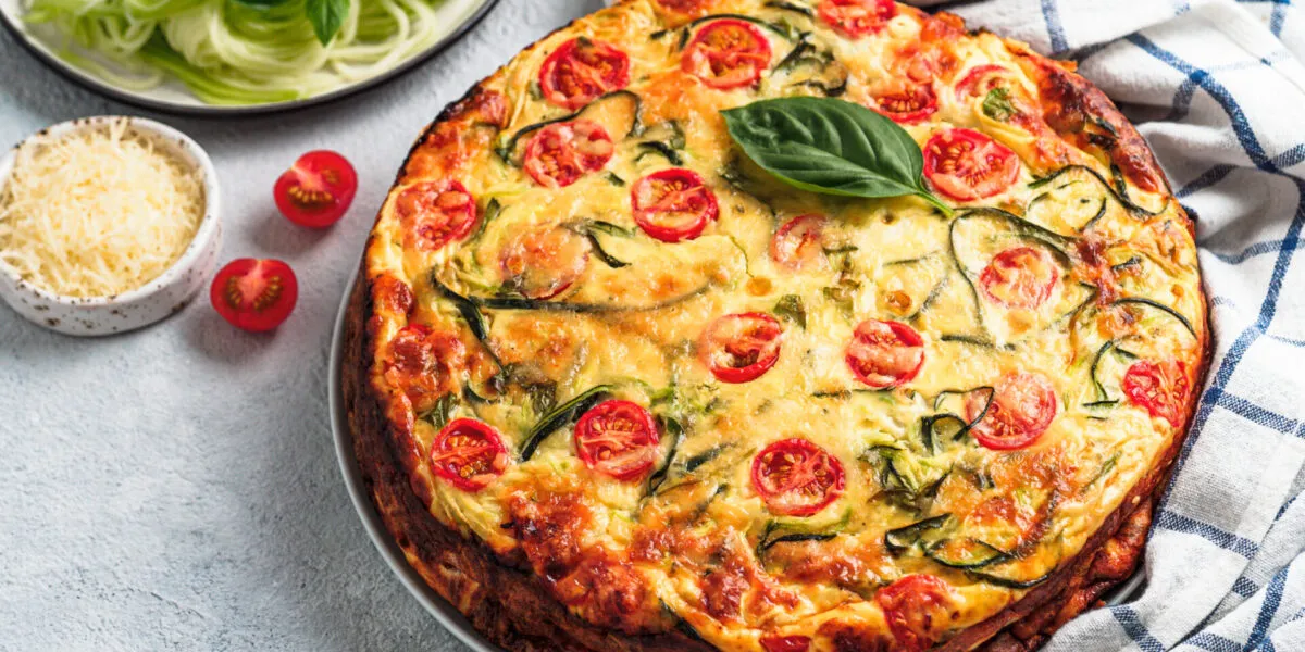 Torta salata fit con zucchine, pomodorini e basilico fresco, servita su un piatto.