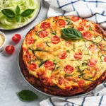 Torta salata fit con zucchine, pomodorini e basilico fresco, servita su un piatto.