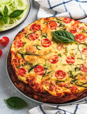 Torta salata fit con zucchine, pomodorini e basilico fresco, servita su un piatto.